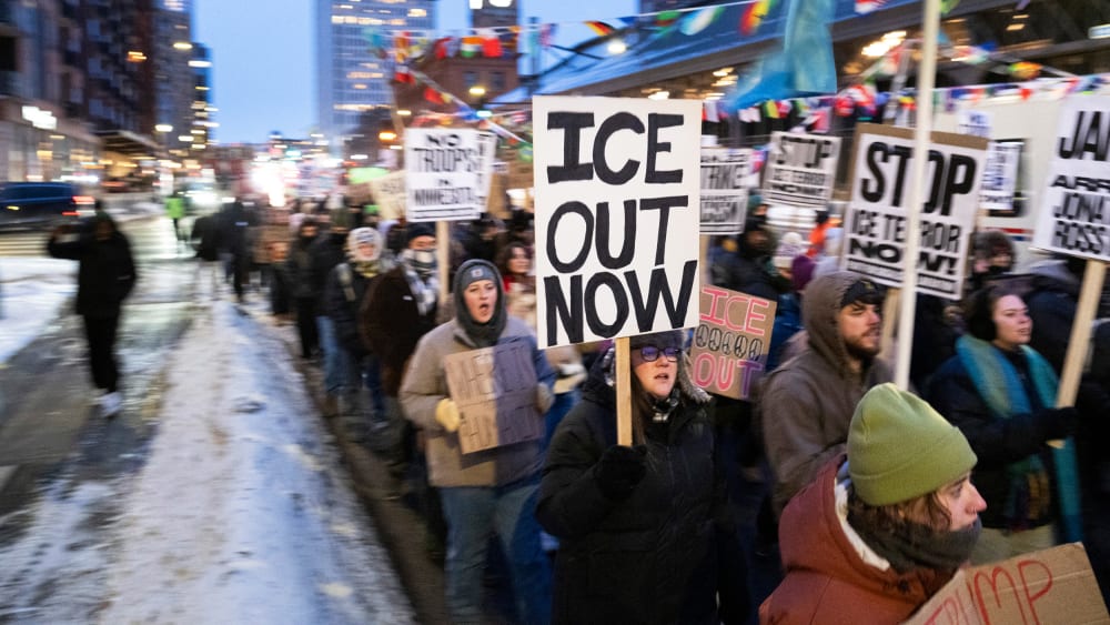 People holding picket signs against ICE march in the street.