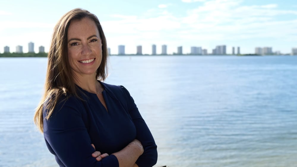 Emily Gregory poses for a photo with her arms crossed in front of a body of water.