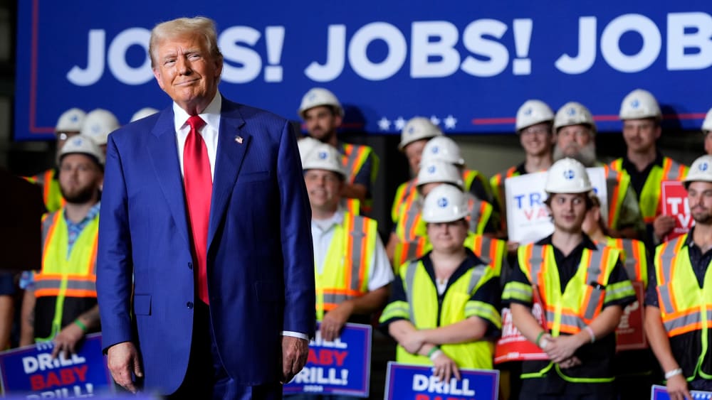 Donald Trump smirks in front of people in hard hats and yellow vests holding signs that say "DRILL BABY DRILL!" Behind them, a large poster that reads "JOBS! JOBS! JOBS!"