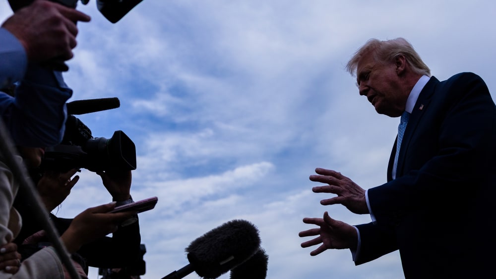 In this photo shot from below, journalists with mics and recorders can be seen on the left as Donald Trump speaks to them as he makes a gesture with his hands.