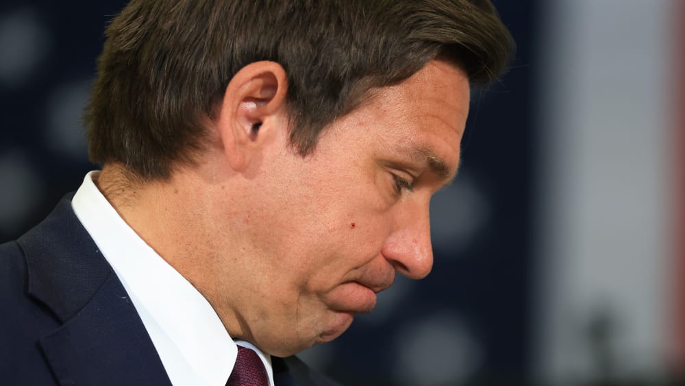 Ron DeSantis, seen in profile, bites his lips with his head down.