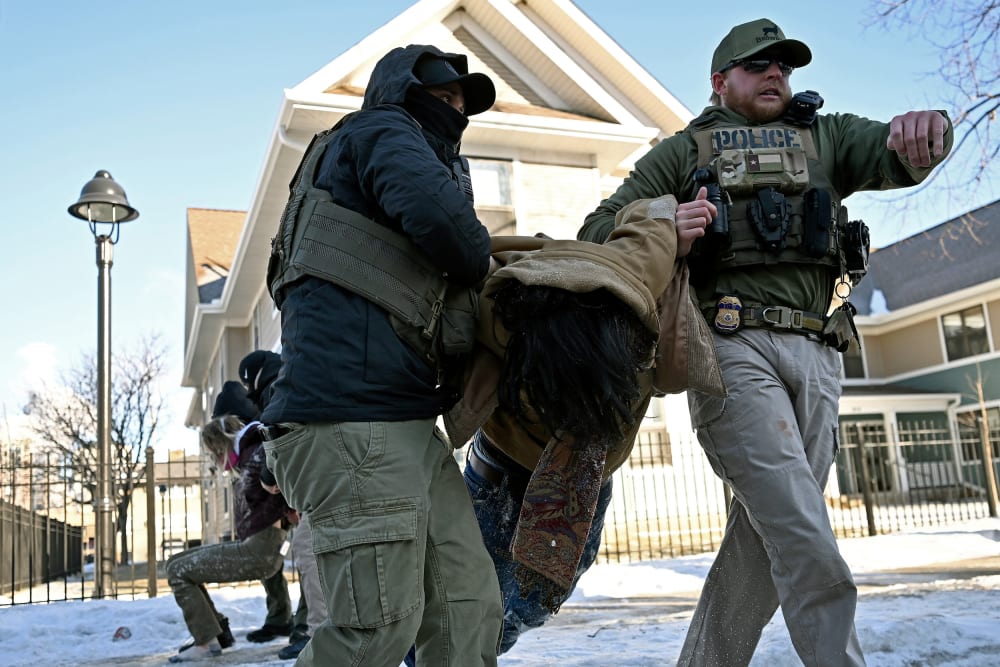 Multiple federal agents drag two people by the arms.