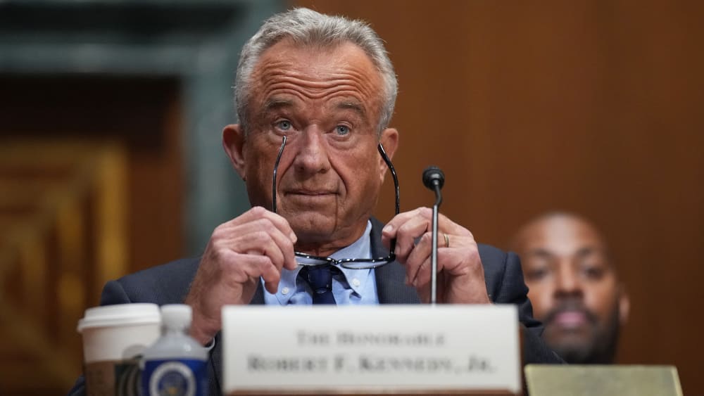 RFK Jr. raises his eyebrows with his glasses in his hands.