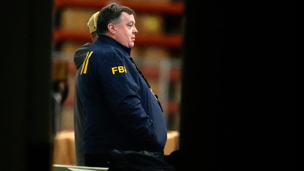 An FBI agent is seen standing near green boxes.