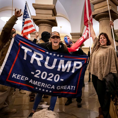People within the Capitol hold flags supporting Donald Trump.
