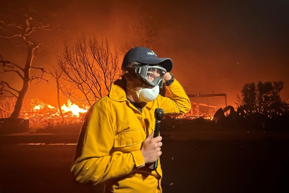 MS NOW's Jacob Soboroff stands with a microphone, wearing a face mask as Palisades fire continues in the background.