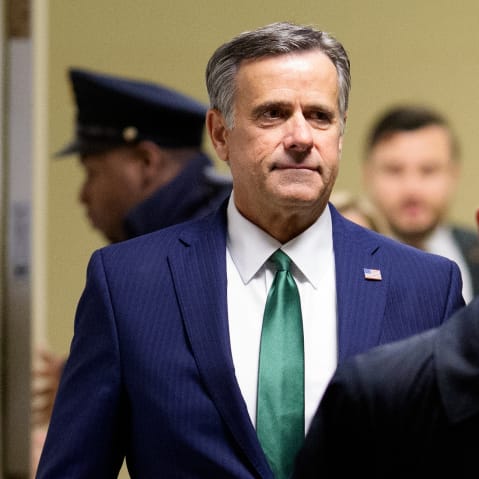 John Ratcliffe walks down a hallway behind other individuals.
