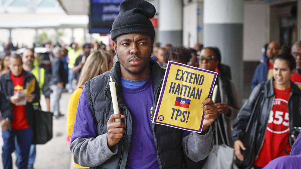 A man holds a candle and a sign about [protection tps for Haitians.