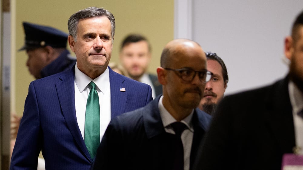 John Ratcliffe walks down a hallway behind other individuals.