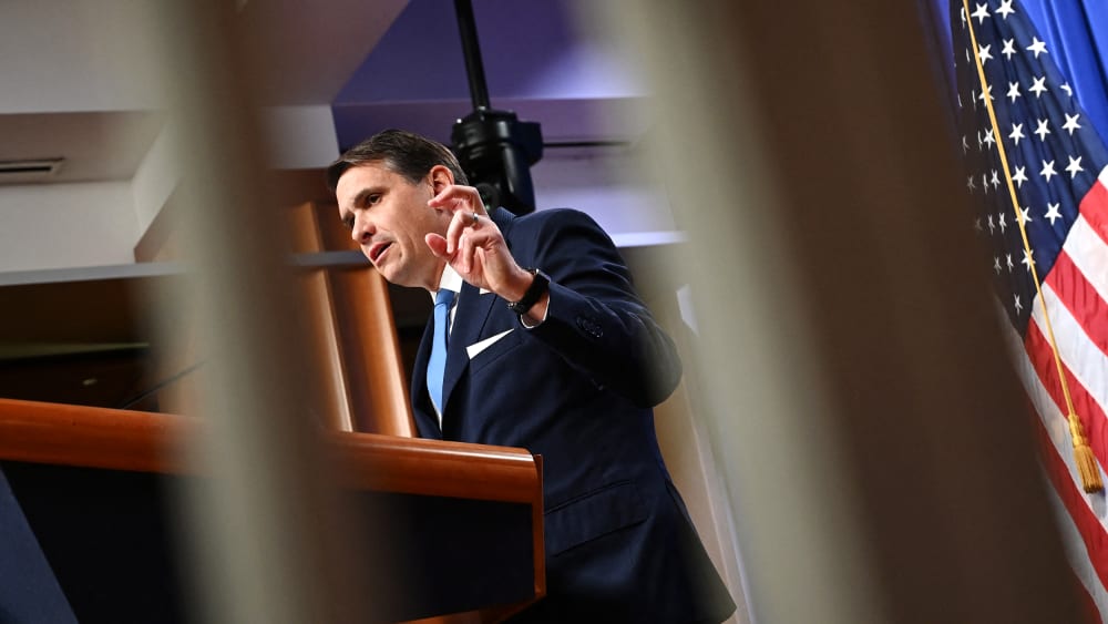 Todd Blanche is seen through two white bars as he speaks at a presser.