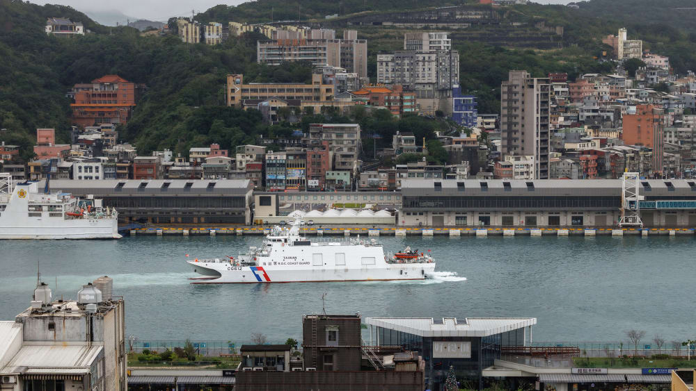 A coast guard ship sails through a body of water surrounded by a city.