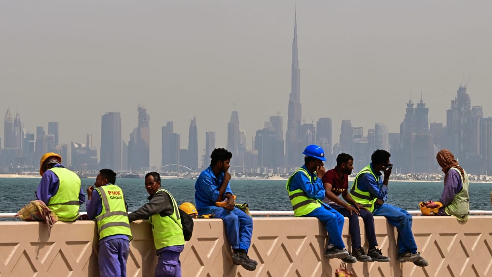 Workers sit on a wall against the Dubai backdrop of the city skyline as they take a break.