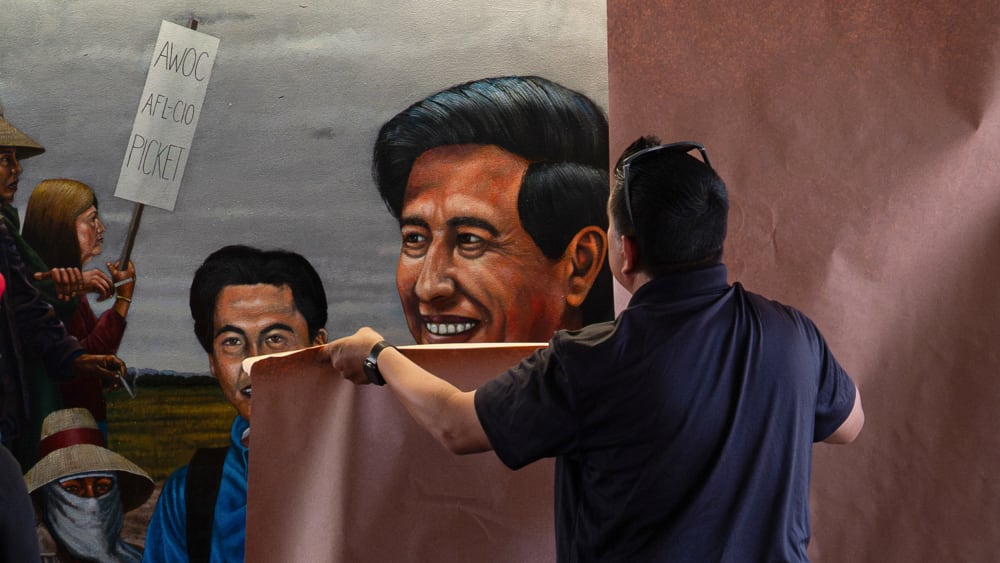 A person puts brown paper on top of a mural featuring Cesar Chavez.