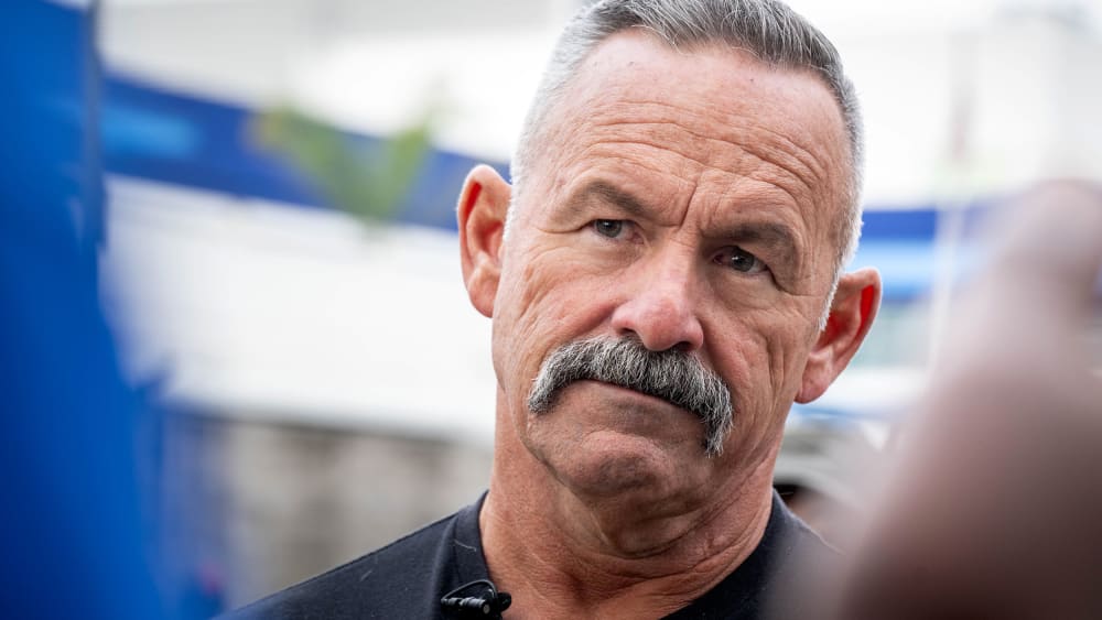 Chad Bianco looks on as he listens to another person.