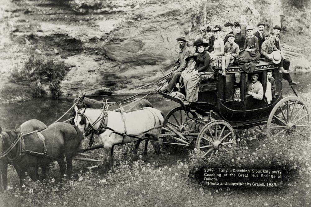 A large group of people ride in and on top of a stagecoach, Hot Springs, South Dakota, 1889.