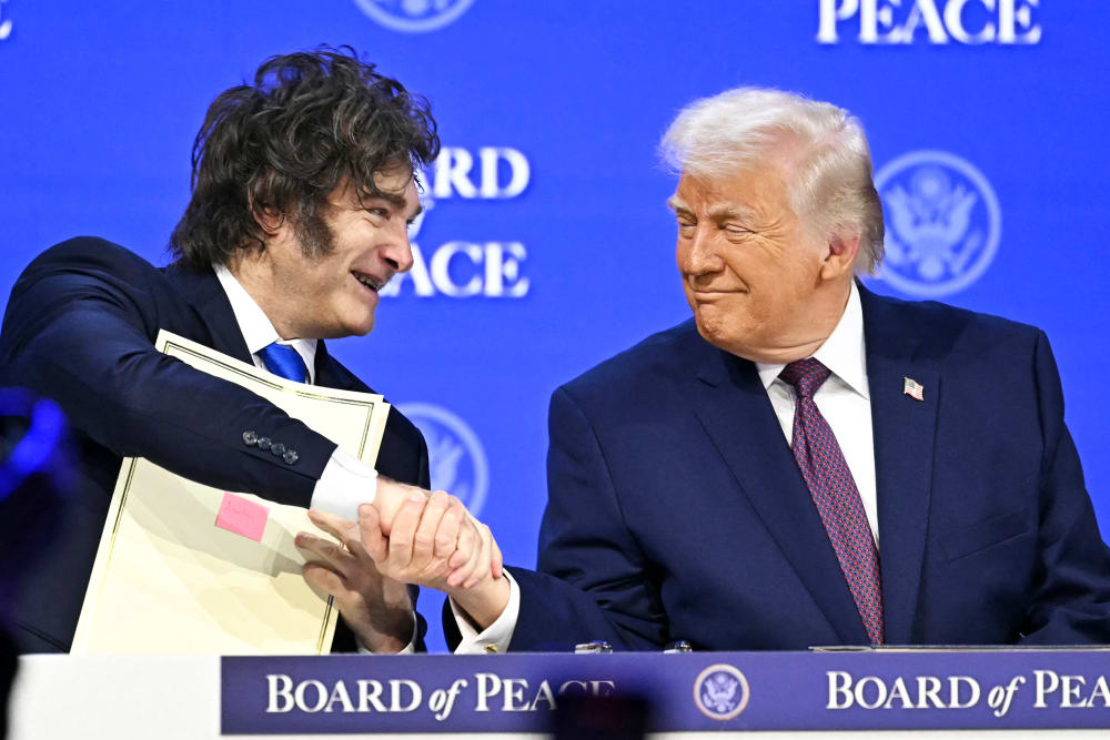 Javier Milei , left, shakes hands with Donald Trump while sitting at a table.