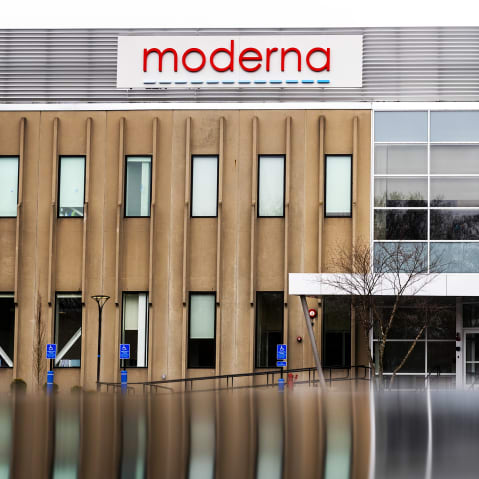 Moderna hq building seen with the red logo. Bottom of the frame shows a reflection of the building potentially on a puddle of water.