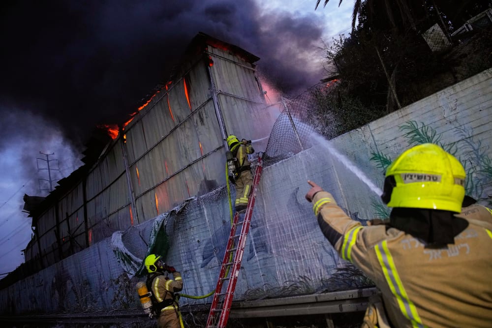 Firefighters try to extinguish flames at the site of a direct hit by an Iranian missile.
