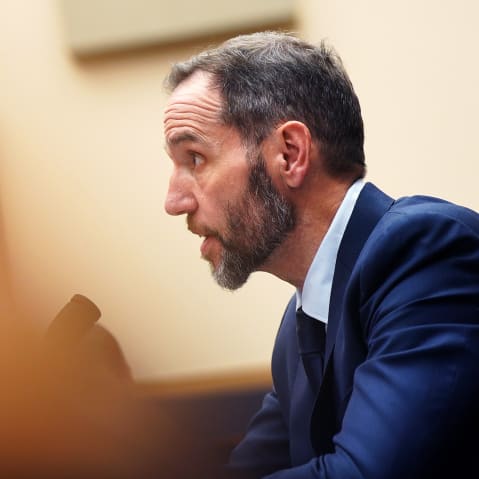 Jack Smith is talking in a tilted frame. What is in front of him is obscured by an out of focus object.