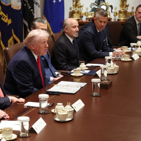 Donald Trump, sitting at the center of the group, speaks while his cabinet members to his left and right listen.