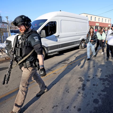 An armed police officer walks as other civilian people follow him.