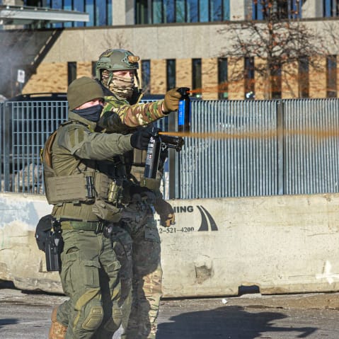 Federal agents use pepper spray against a protester holding a sign during an enforcement operation outside the Whipple Building in Minneapolis.