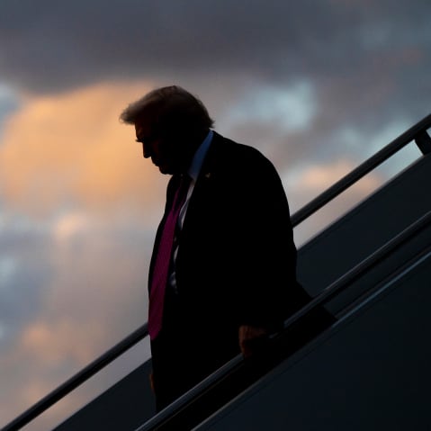 Donald Trump, silhouetted, descends an outdoor staircase. A sky full of colorful clouds is behind him.