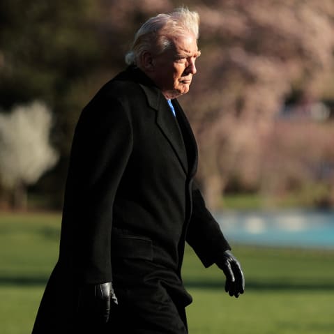 Donald Trump walks at sunset toward the White House building.