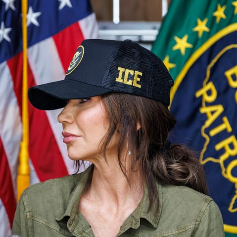Kristi Noem in an ICE hat in front of an American flag and a U.S. Border Patrol flag.