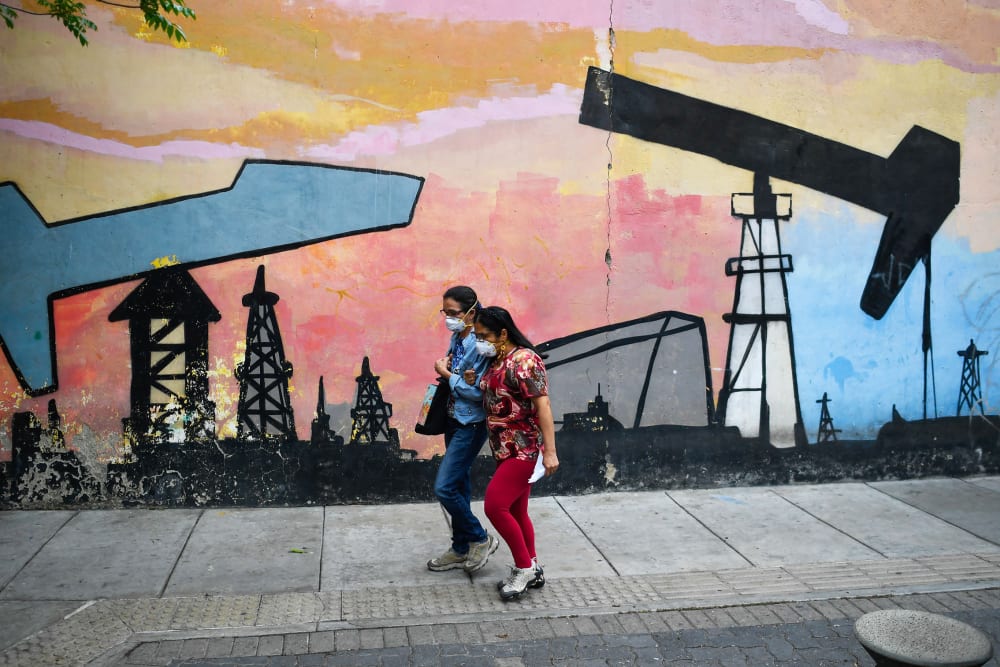 Women walk past a mural depicting an oil pump on April 14, 2021 in a street of Caracas, Venezuela.