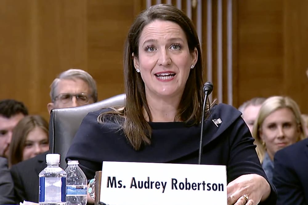 Audrey Robertson sitting at a table with a microphone behind a name tag.