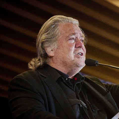 In this photo shot from below, Steve Bannon is seen lifting his left hand pointing in the air as he speaks at the podium.