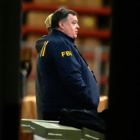 An FBI agent is seen standing near green boxes.
