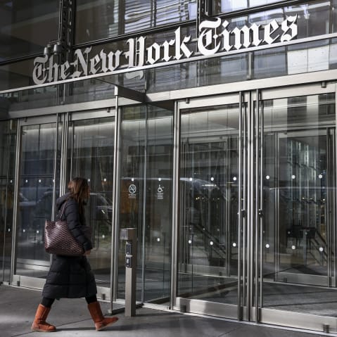 A woman walks into the New York Times building where we can fully see the building sign in the frame.