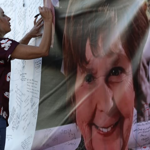 A woman on the left writes on a banner that has Nancy Guthrie's picture on the right.