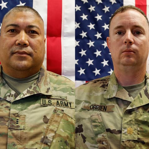 Two people in army uniforms in front of American flags.
