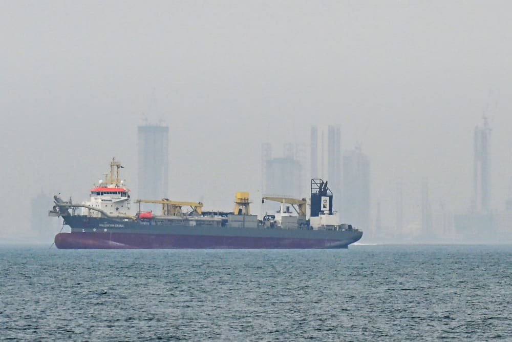 A ship is seen in the foreground and the skyline is seen in the background in fog.