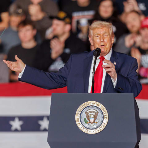 Donald Trump gestures behind a podium in front of an audience.