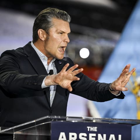 Hegseth speaks at the podium making gestures with his face and hands.