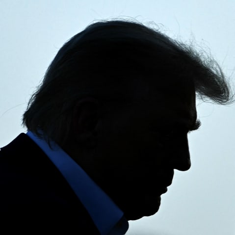 Trump's profile is seen as he walks up to the place. A security person stands on the right side.