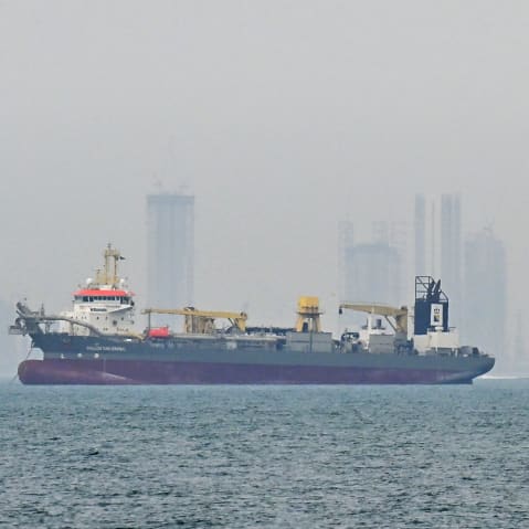 A ship is seen in the foreground and the skyline is seen in the background in fog.
