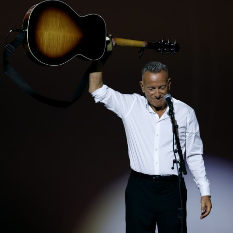 Bruce Springsteen holds a guitar above his head.