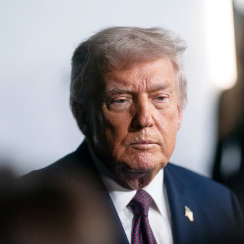 A tight shot shows Donald Trump looking at the reporters and Melania Trump can be seen in the background very out of focus.
