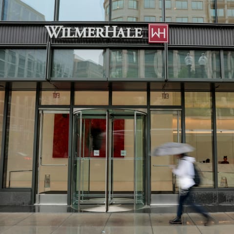A person with an umbrella, blurred in motion, walks past an office building with WilmerHale's name and logo on the facade.