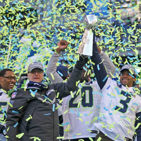 Paul Allen, left, and Russell Wilson hoist the Lombardi trophy in the air as blue and green confetti falls around them.
