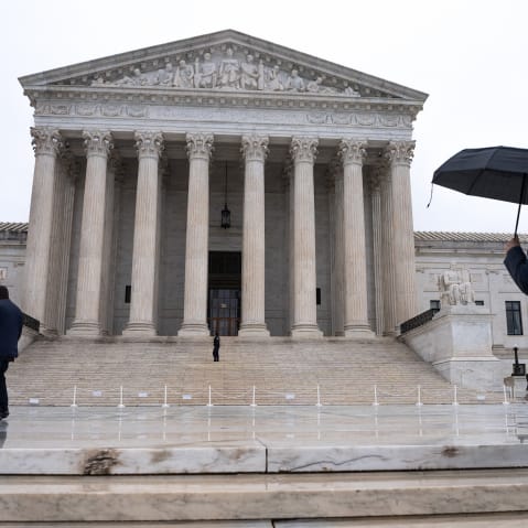 A person with a black umbrella walks past the SCOTUS building in the rain.