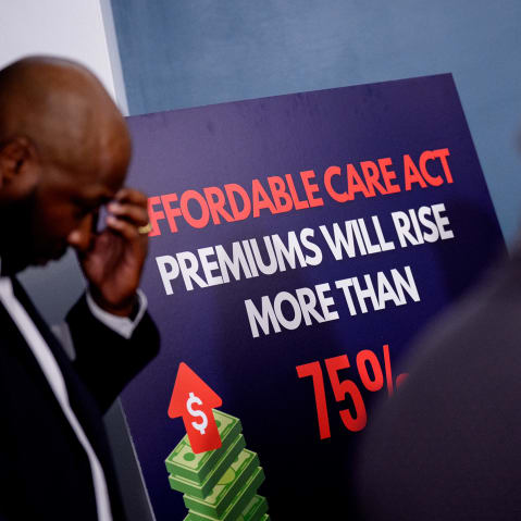 People stand next to a sign that reads "Affordable Care Act Premiums Will Rise More Than 75%."