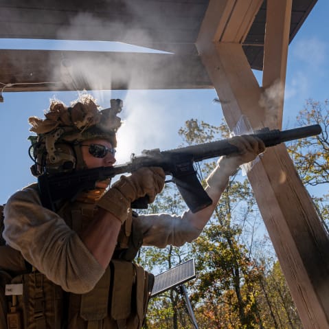 A person, backlit, shoots a gun.