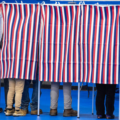 Legs are seen below red, white and blue voting booth curtains.