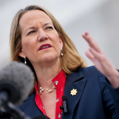 Kris Mayes gestures in front of a microphone.